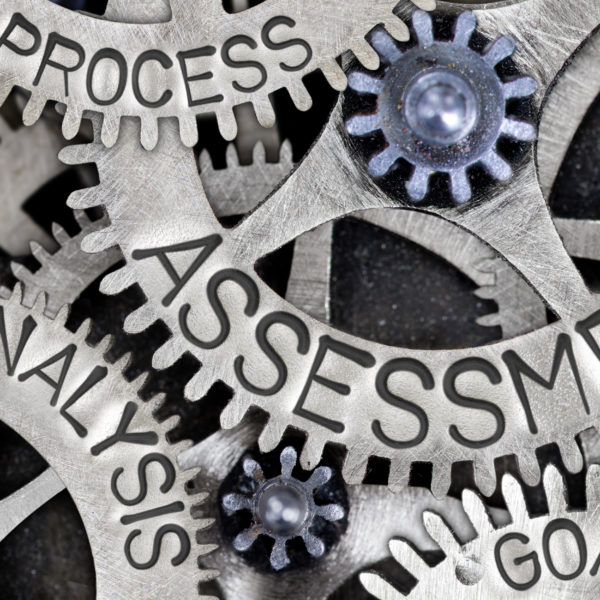 Macro photo of tooth wheel mechanism with ASSESSMENT, PLAN, ANALYSIS, PROCESS, GOAL, METHOD and SYSTEM words imprinted on metal surface